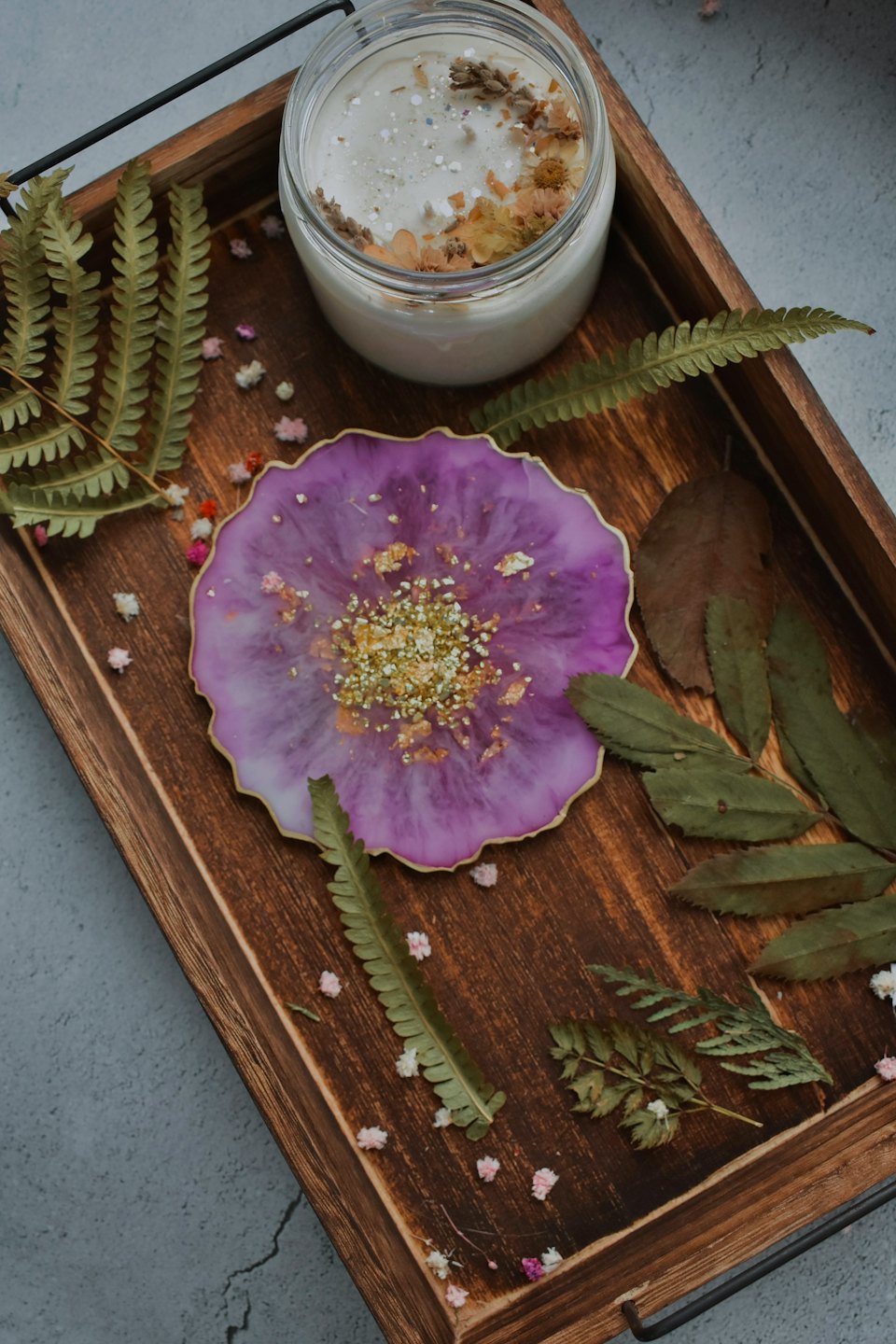 A decorative candle and resin coaster sit on a wooden tray.